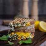 Knuspriges Grilled Cheese Sandwich mit geschmolzenem Käse, cremigem Spinat und Tomate auf Holzbrett serviert