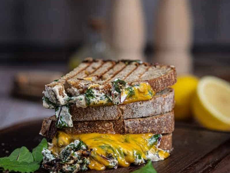 Knuspriges Grilled Cheese Sandwich mit geschmolzenem Käse, cremigem Spinat und Tomate auf Holzbrett serviert