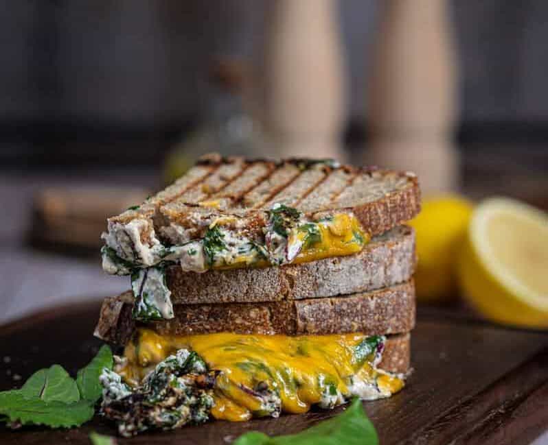 Knuspriges Grilled Cheese Sandwich mit geschmolzenem Käse, cremigem Spinat und Tomate auf Holzbrett serviert