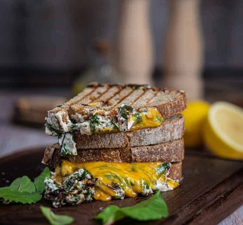 Grilled Cheese Sandwich mit Spinat, Tomate und Cheddar frisch gegrillt Knuspriges Grilled Cheese Sandwich mit geschmolzenem Käse, cremigem Spinat und Tomate auf Holzbrett serviert