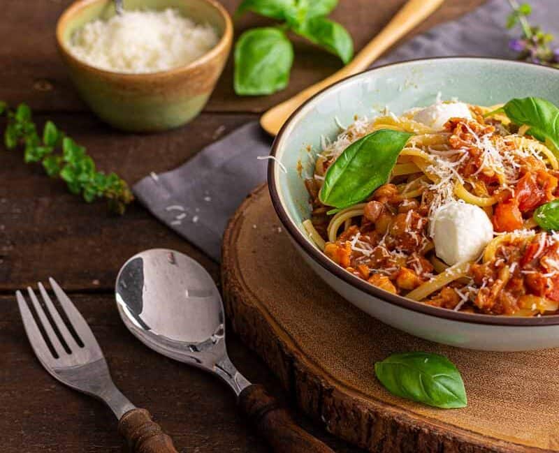 Nahaufnahme einer dampfenden Linsenbolognese mit roten Linsen auf Spaghetti, serviert in einer weißen Schale mit frischen Kräutern