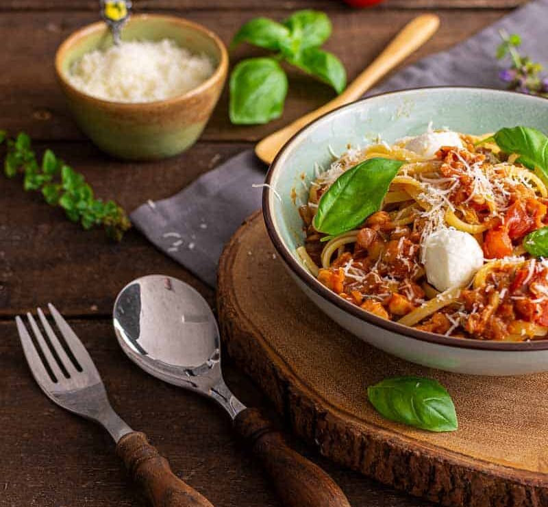 Vegetarische Linsenbolognese mit roten Linsen auf Spaghetti Nahaufnahme einer dampfenden Linsenbolognese mit roten Linsen auf Spaghetti, serviert in einer weißen Schale mit frischen Kräutern