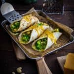 Vegetarische Wraps gefüllt mit Brokkoli, geschmolzenem Käse und cremigem Cashew-Topping, angerichtet als gesundes Fingerfood auf einem Teller